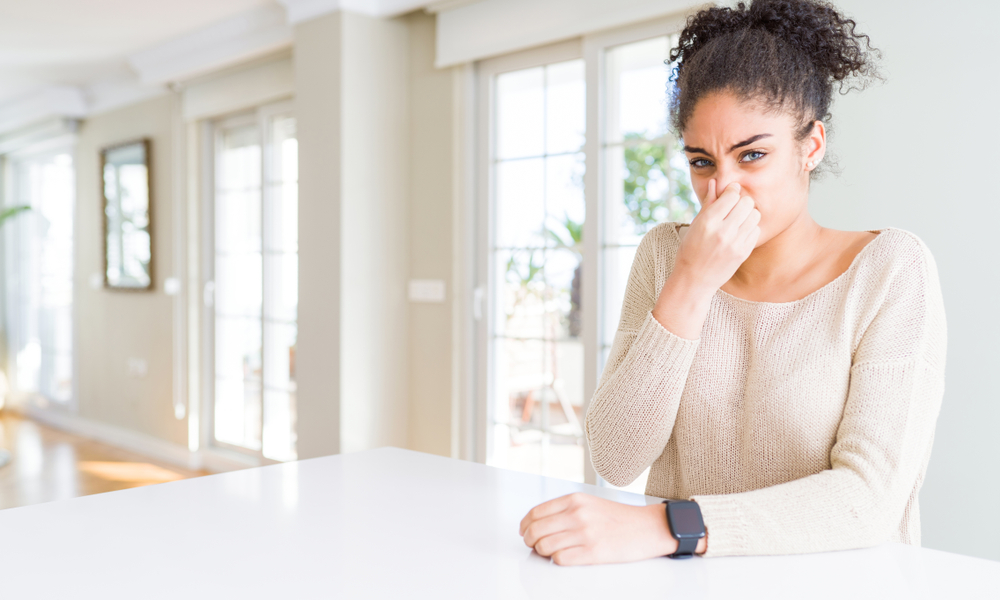 woman holds her nose after smelling something bad insider her home