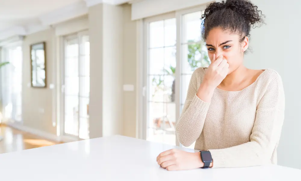Woman holds her nose after smelling something bad inside her home.