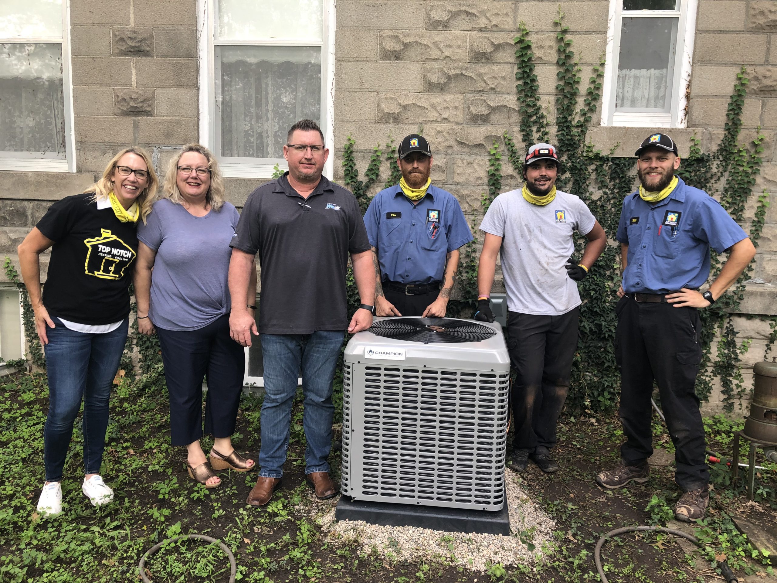 The Top Notch Heating, Cooling & Plumbing team posing in front of a client's home and A/C unit.