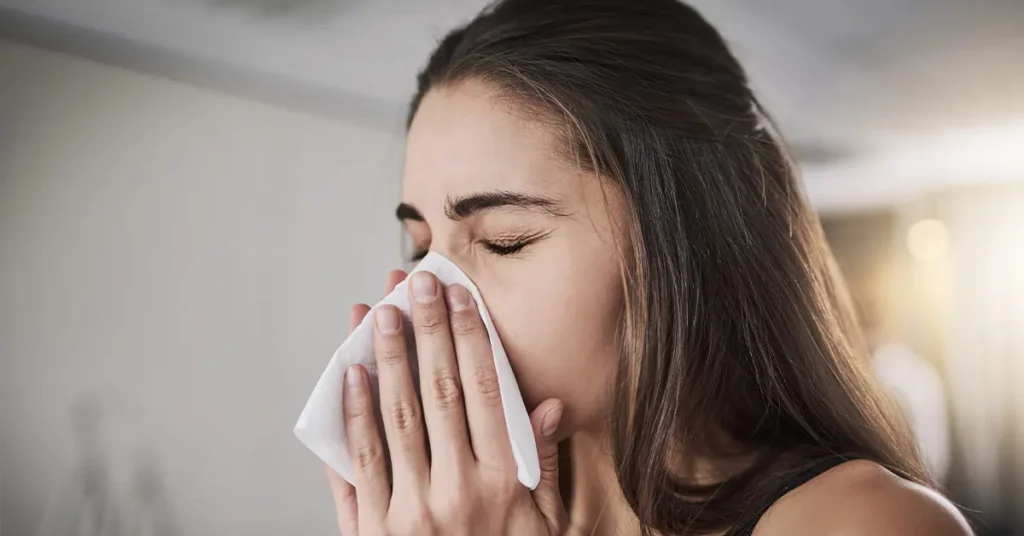A woman mid-sneeze with a tissue to her nose.