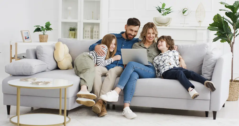 A family sitting together on a living area couch, viewing a laptop screen.