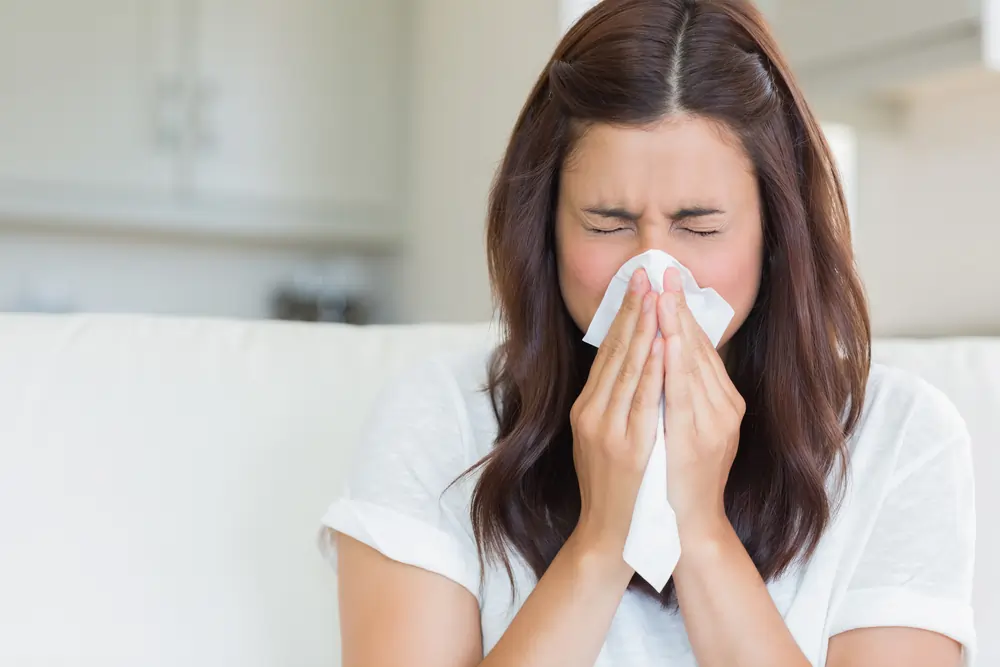 A woman blowing her nose with a tissue.