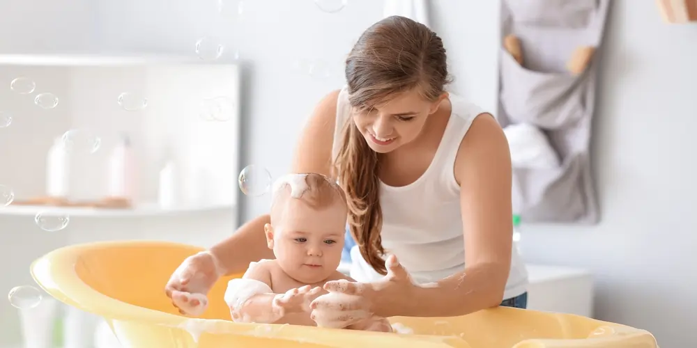 A woman giving her child a bath in a small yellow tub with bubbles.