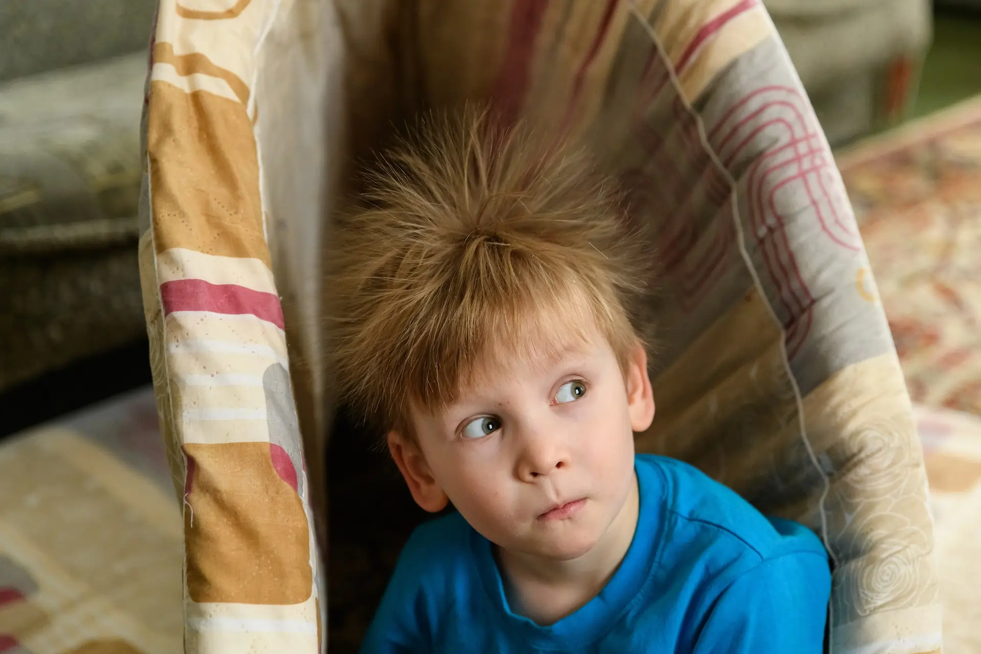 A seated child with static electricity surrounding his hair, causing it to stand on end.