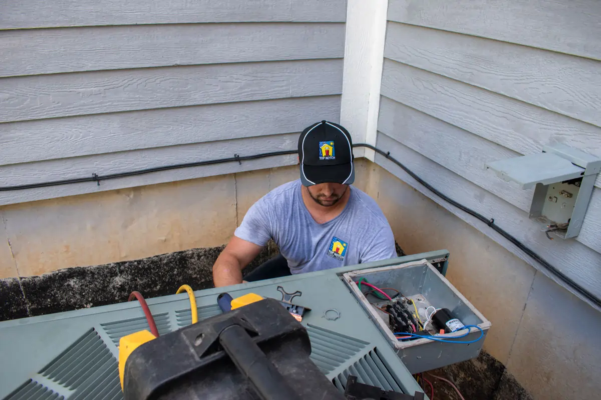 A Top Notch Heating, Cooling & Plumbing technician performing work on a customer's outdoor a/c unit.