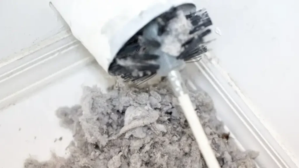 Debris and lint on the ground outside of a dryer's ventilation piping while it's being cleaned.