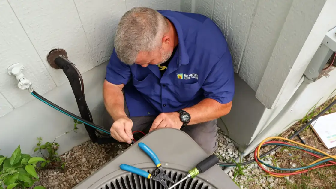 A Top Notch Heating, Cooling & Plumbing technician performing repairs on a Kansas City home’s exterior AC unit. 