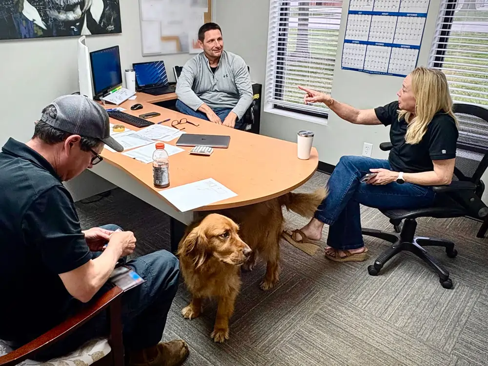 The Top Notch Heating, Cooling & Plumbing office interior, featuring staff members and Finn the dog during a meeting.