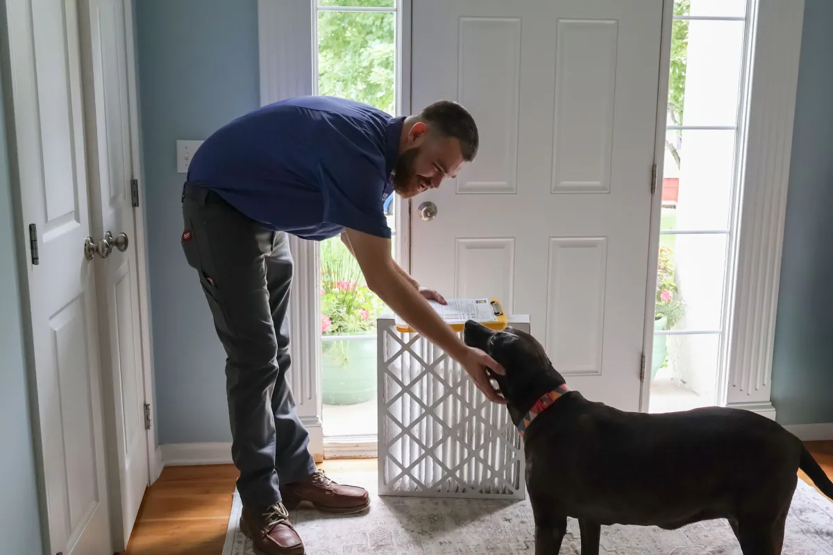 Top Notch Heating, Cooling & Plumbing VIP Priority Club air filter replacement Top Notch Heating, Cooling & Plumbing technician greeting a dog with an air filter